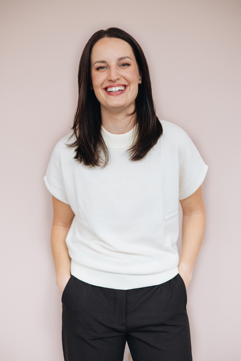 Maja Fenn lächelt freundlich und verschränkt die Arme, vor einem warmen, hellen Hintergrund.