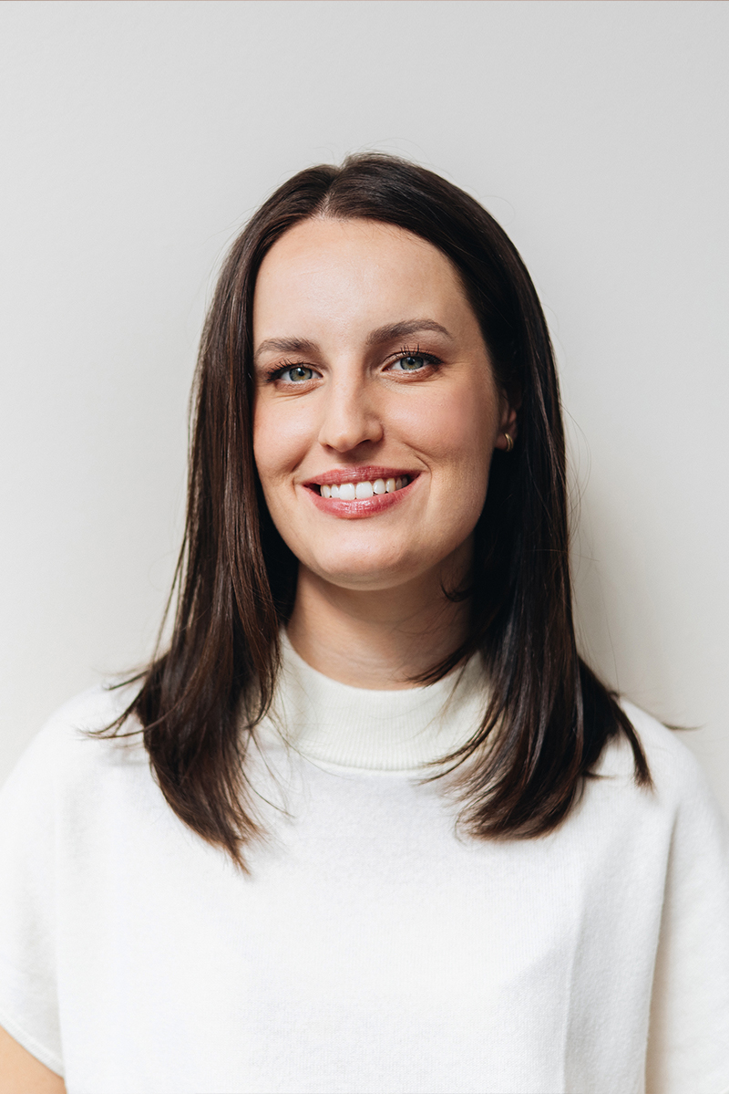 Maja Fenn lächelt freundlich und verschränkt die Arme, vor einem warmen, hellen Hintergrund.